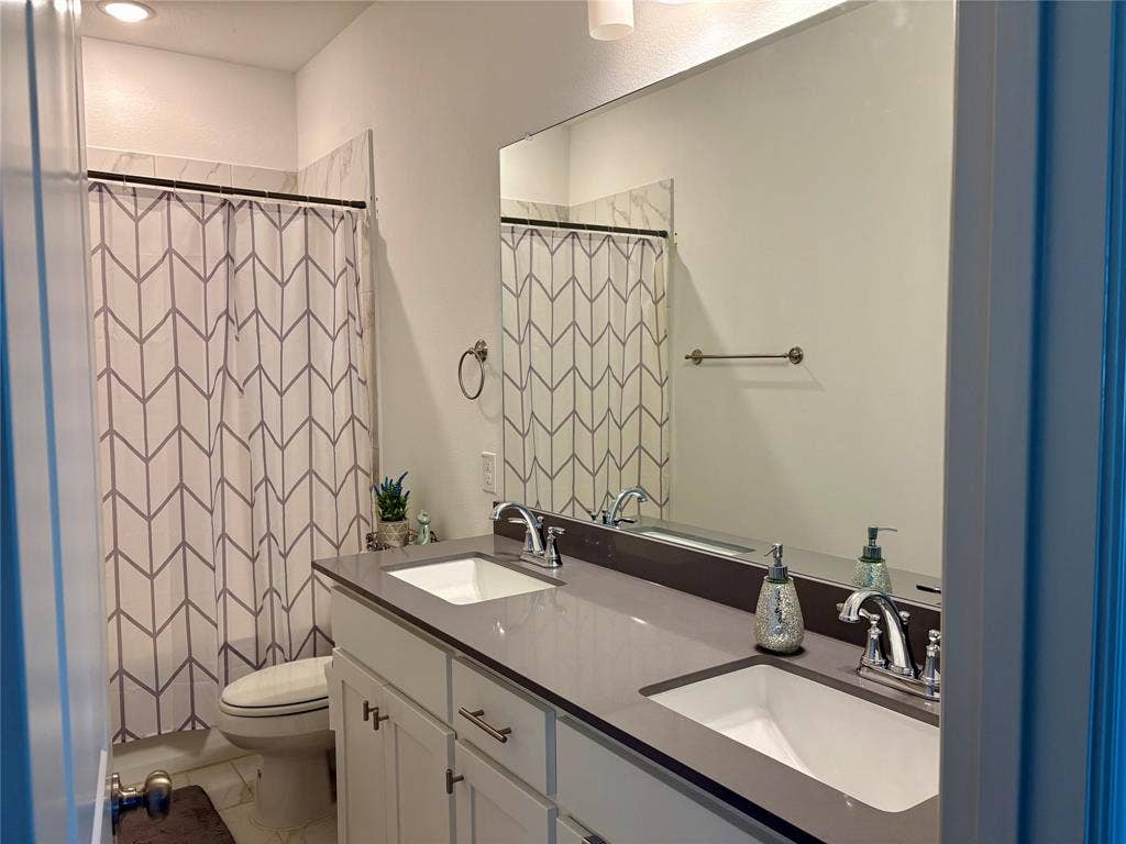9096 Phoebe Road, Frisco, TX 75035 Dual-sink vanity with a solid-surface countertop, undermount sinks, and polished chrome fixtures paired with a full-width vanity mirror
