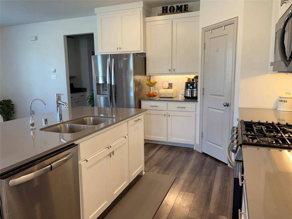 9096 Phoebe Road, Frisco, TX 75035 Kitchen featuring white shaker-style cabinetry, quartz countertops, stainless steel appliances, a central island with an undermount sink, and wood-finish flooring