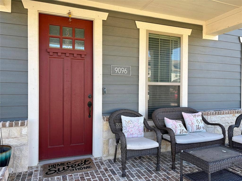 9096 Phoebe Road, Frisco, TX 75035 Covered porch featuring horizontal lap siding, stone veneer accents, a red paneled entry door with a multi-pane glass inlay, and brick-patterned flooring