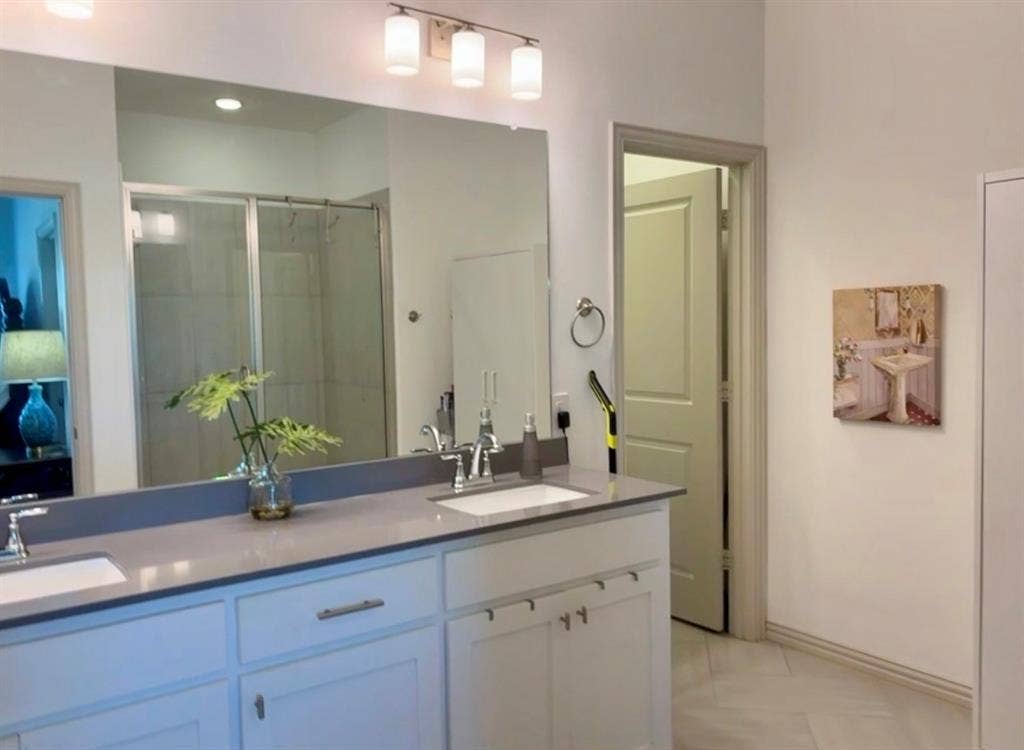 9096 Phoebe Road, Frisco, TX 75035 Dual-sink vanity with a solid-surface countertop, full-width mirror, and three-light wall-mounted fixture