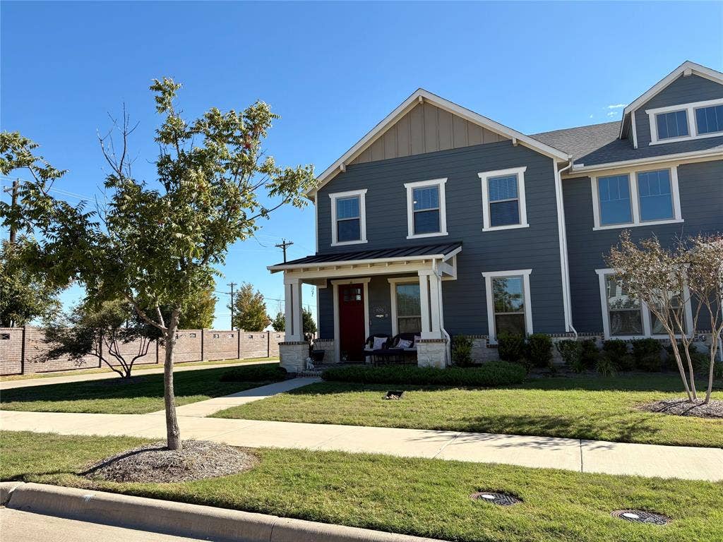 9096 Phoebe Road, Frisco, TX 75035 Two-story residence featuring blue horizontal lap siding, stone veneer accents, a covered front porch with tapered columns, a metal roof accent, and a solid-color entry door