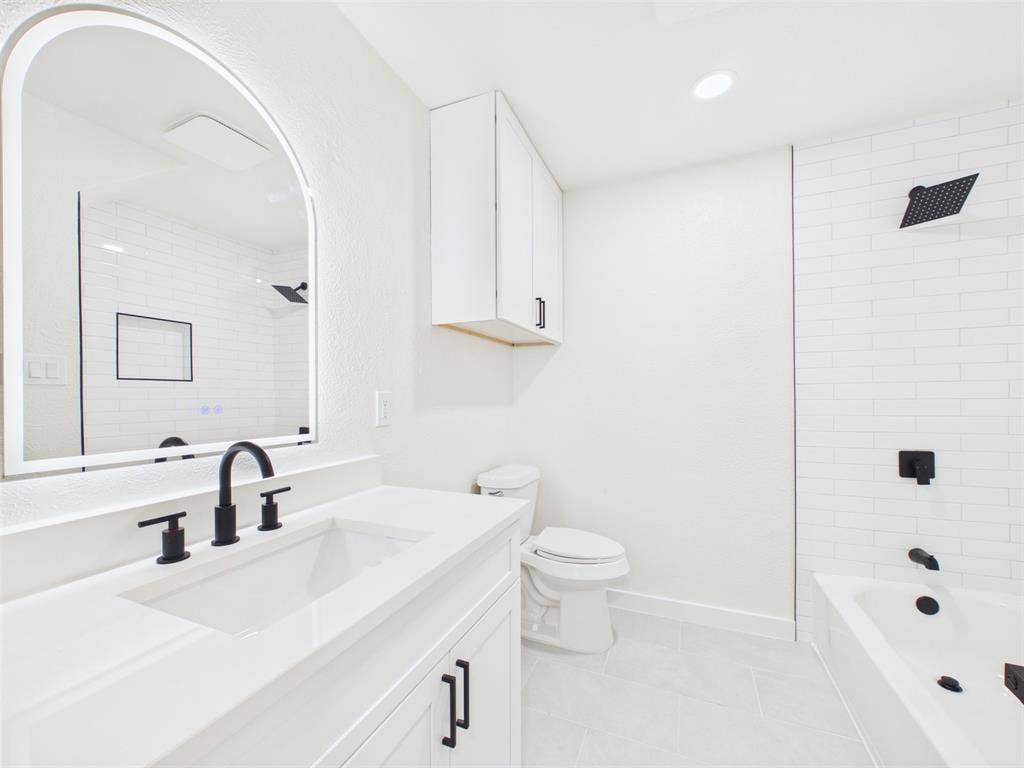 Bathroom featuring an arched LED vanity mirror, white cabinetry with matte black hardware, subway tile shower surround, and matte black plumbing fixtures
