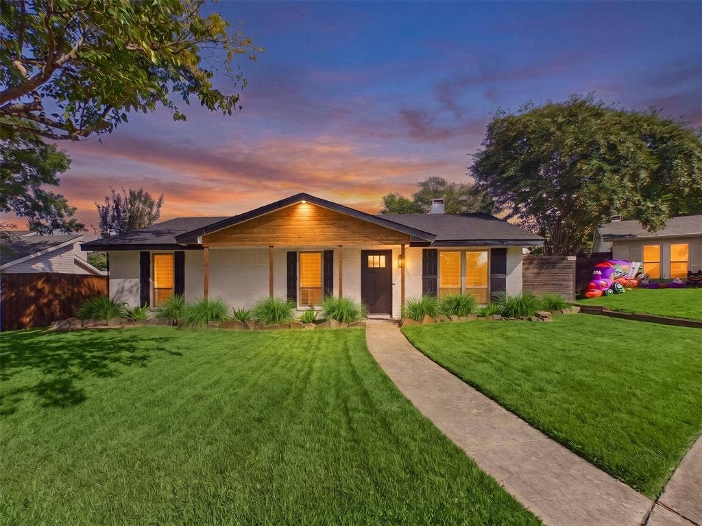 Single-story exterior featuring a light-toned stucco façade, natural wood-accented gable, concrete walkway, and decorative exterior shutters