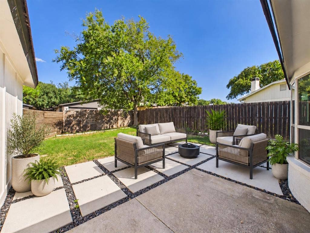 Rear patio featuring large square concrete pavers, decorative dark stone borders, and wood privacy fencing