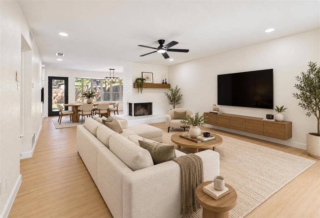 Living area featuring light-toned wood-finish flooring, a white-painted brick corner fireplace with a natural wood mantel, recessed lighting, and a modern ceiling fan