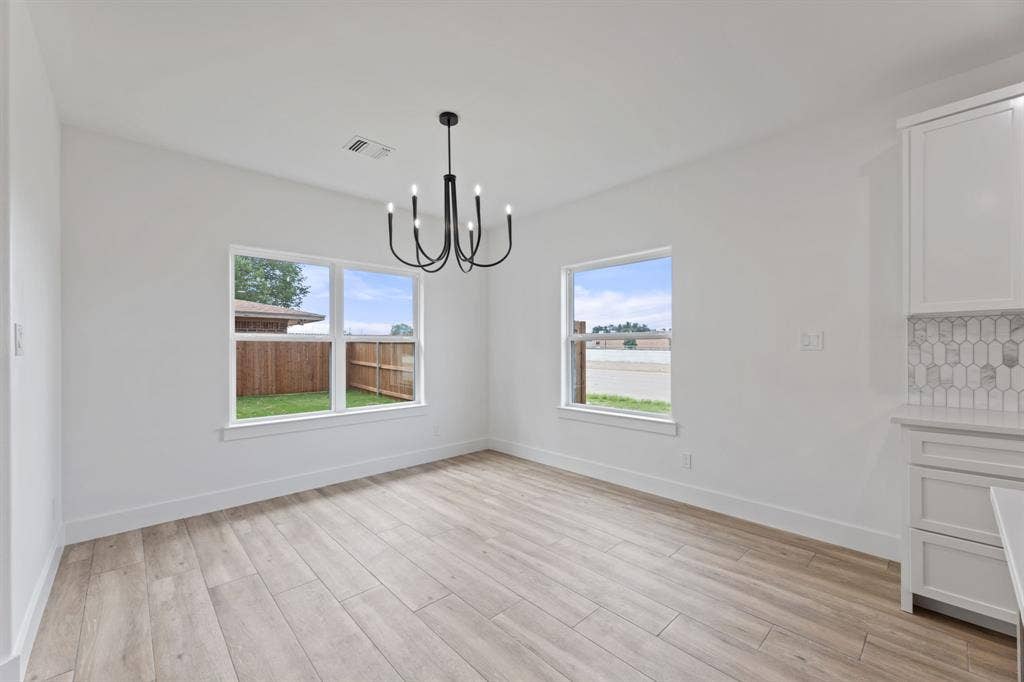 Unfurnished dining area featuring baseboards, visible vents, light wood-style floors, and a chandelier