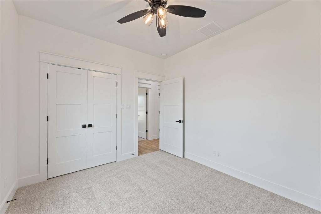 Unfurnished bedroom featuring a closet, carpet floors, baseboards, visible vents, and ceiling fan