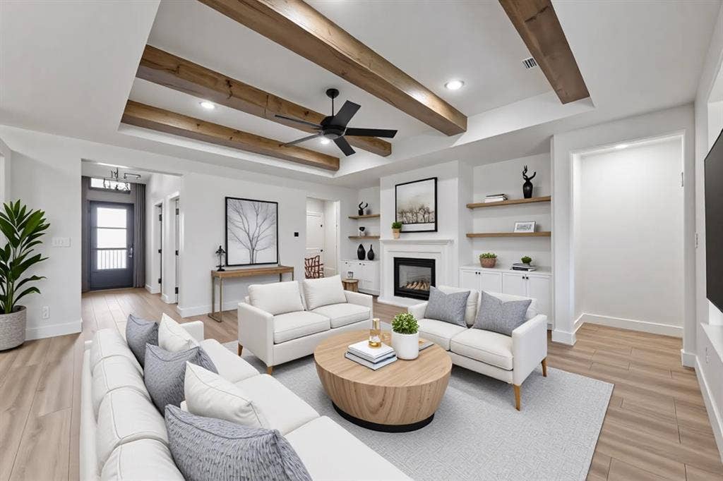 Living room with a tray ceiling, a glass covered fireplace, light wood finished floors, and a ceiling fan