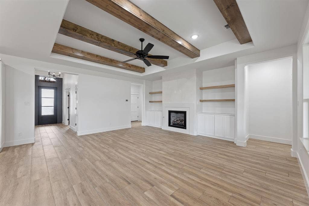 Unfurnished living room featuring beam ceiling, ceiling fan with notable chandelier, baseboards, and light tile finished floors