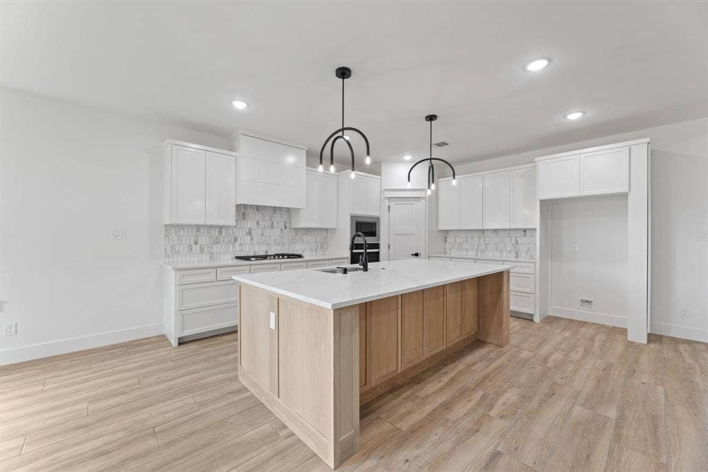Kitchen featuring a large island with sink, a sink, appliances with stainless steel finishes, light wood-style flooring, and white cabinets
