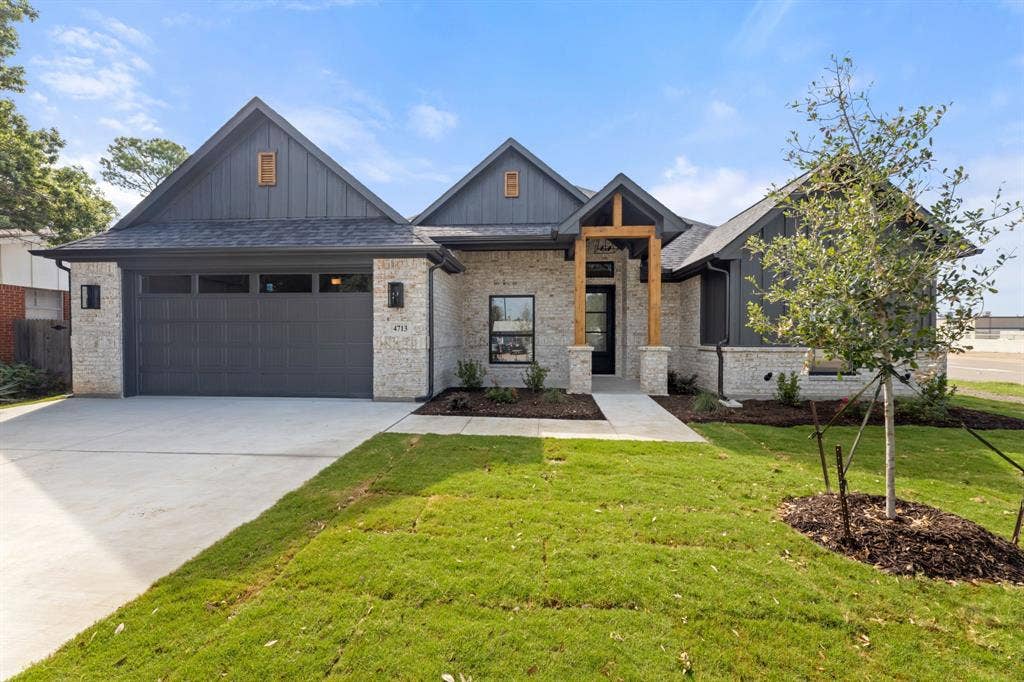 View of front of home with an attached garage, concrete driveway, a front lawn, board and batten siding, and a shingled roof