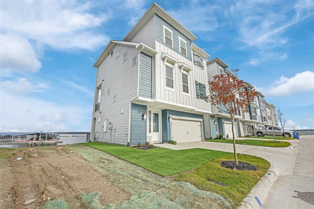 View of front of property with board and batten siding, concrete driveway, an attached garage, and a front lawn