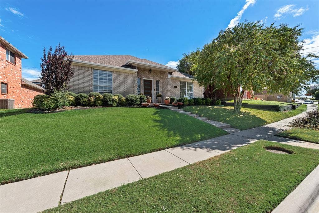 4104 Creekmeadow Drive, Carrollton, TX 75010 Single-story brick exterior featuring a hipped roofline, manicured lawn, and mature shade trees