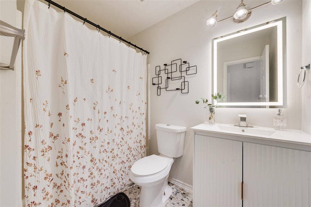 4104 Creekmeadow Drive, Carrollton, TX 75010 Bathroom featuring a vanity with vertical ribbed cabinet doors, a countertop with an integrated basin, a lighted mirror, and decorative wall-mounted metal shelving