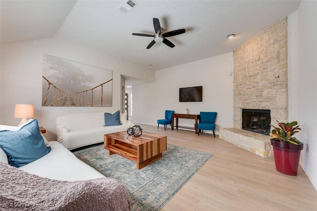 4104 Creekmeadow Drive, Carrollton, TX 75010 Living area featuring high ceilings, wood-finish flooring, and a full-height stone-veneer fireplace with a raised hearth