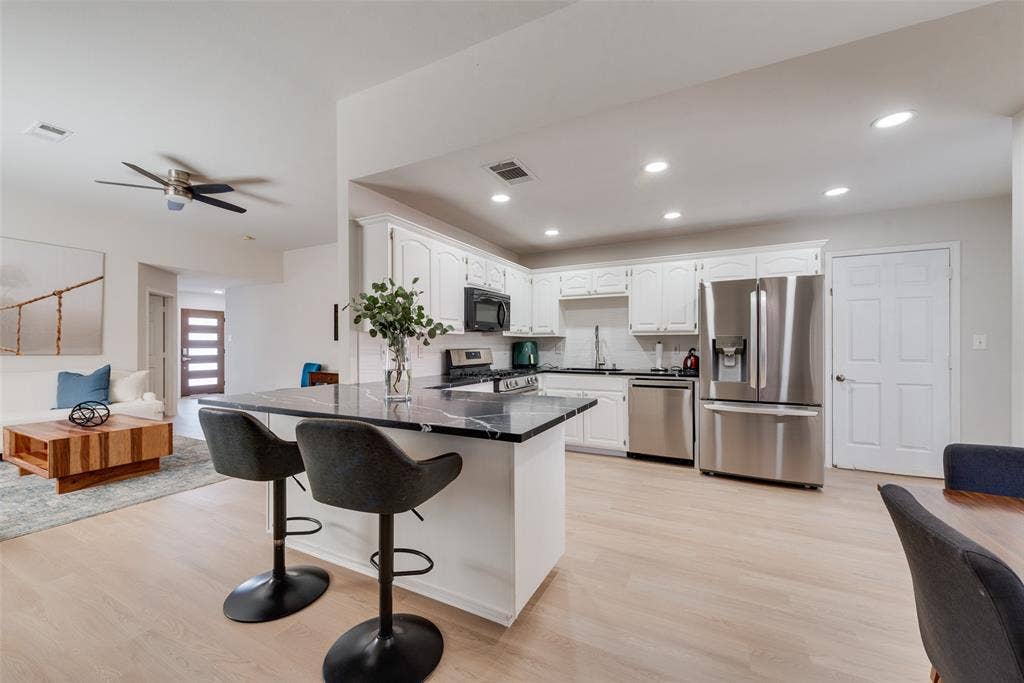 4104 Creekmeadow Drive, Carrollton, TX 75010 Kitchen featuring white cabinetry, dark stone-finish countertops, stainless steel appliances, a center island with a breakfast bar, and wood-finish flooring