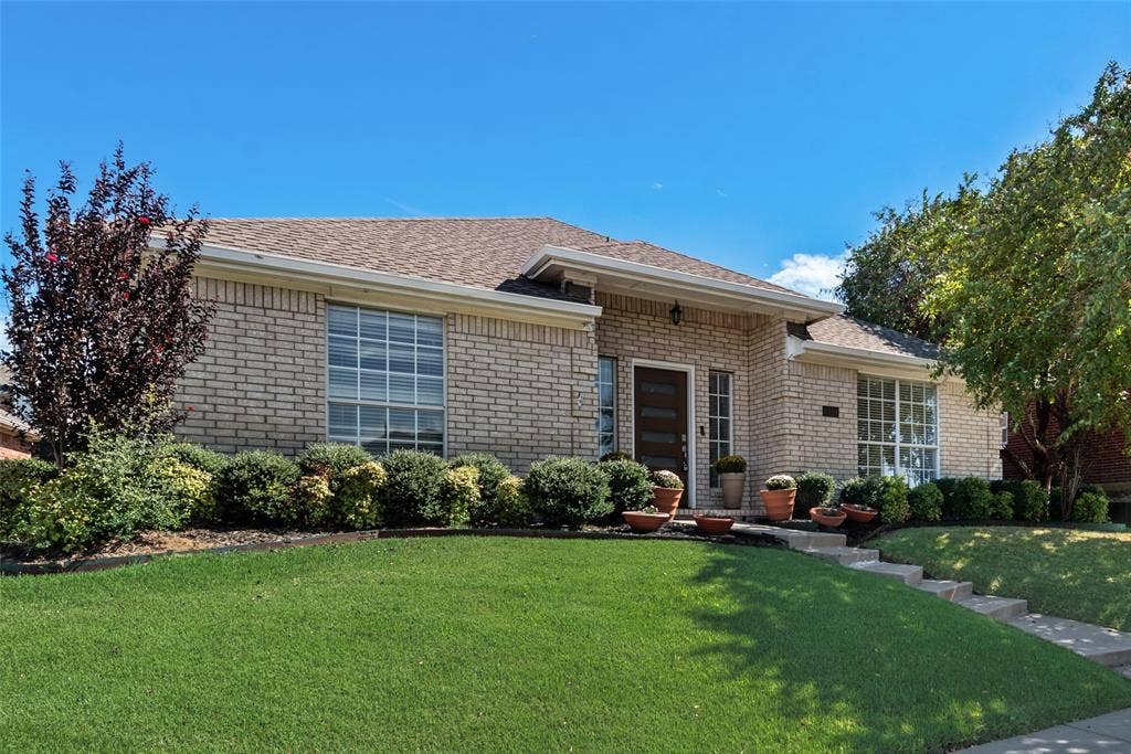 4104 Creekmeadow Drive, Carrollton, TX 75010 Single-story residence featuring a light-toned brick facade, multi-pane windows, a recessed entry with a paneled door, and a multi-level concrete walkway
