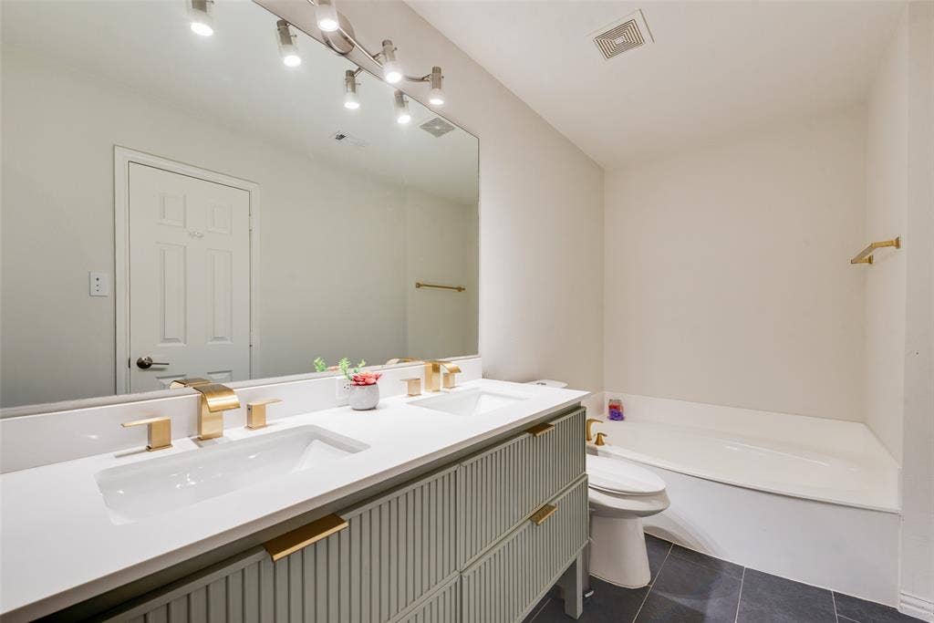 4104 Creekmeadow Drive, Carrollton, TX 75010 Dual-sink vanity with ribbed cabinetry, white countertops, brass-finish fixtures, and a large wall-mounted mirror