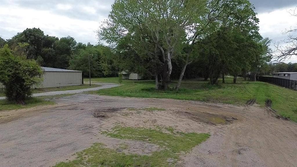 3110 W Gentry Parkway, Tyler, TX 75702 Expansive level lot featuring a metal-sided outbuilding, a gravel driveway, and mature trees