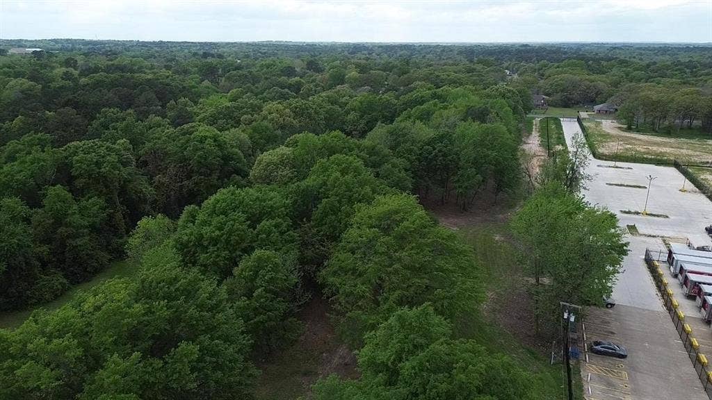 3110 W Gentry Parkway, Tyler, TX 75702 Aerial perspective of a sprawling lot featuring mature tree canopy, dense woodlands, and paved surface parking