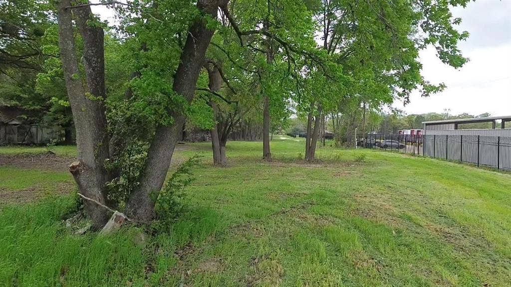 3110 W Gentry Parkway, Tyler, TX 75702 Expansive lot featuring mature trees, natural vegetation, and a metal perimeter fence