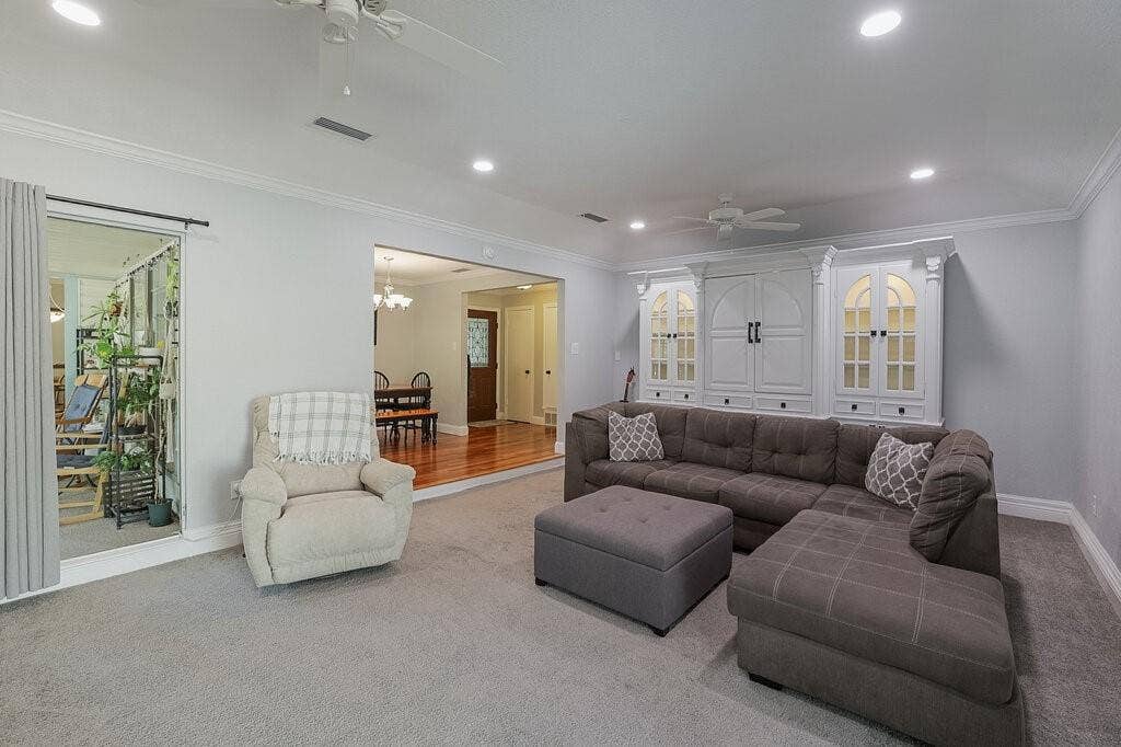 Living area featuring recessed lighting, ceiling fans, crown molding, and a built-in floor-to-ceiling cabinet unit with glass-paneled display doors