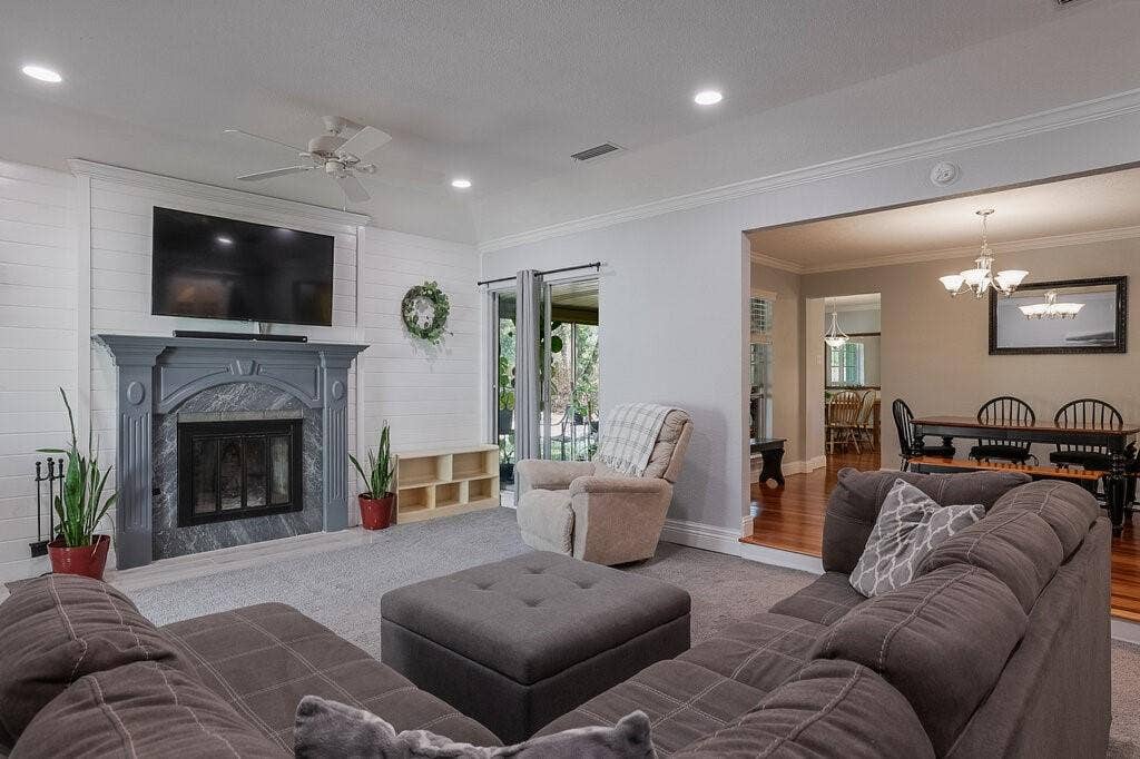 Living space featuring a fireplace with a stone surround, white horizontal wall paneling, crown molding, recessed lighting, and a ceiling fan