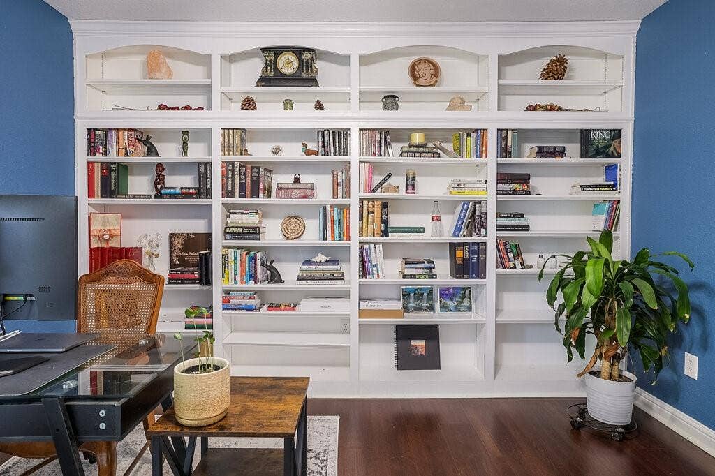 Floor-to-ceiling custom built-in white shelving featuring arched upper detailing and dark wood-finish flooring