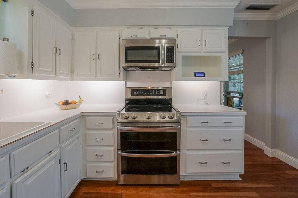 Kitchen featuring white cabinetry, solid-surface countertops, wood-finish flooring, and stainless steel appliances including an over-the-range microwave and a gas range