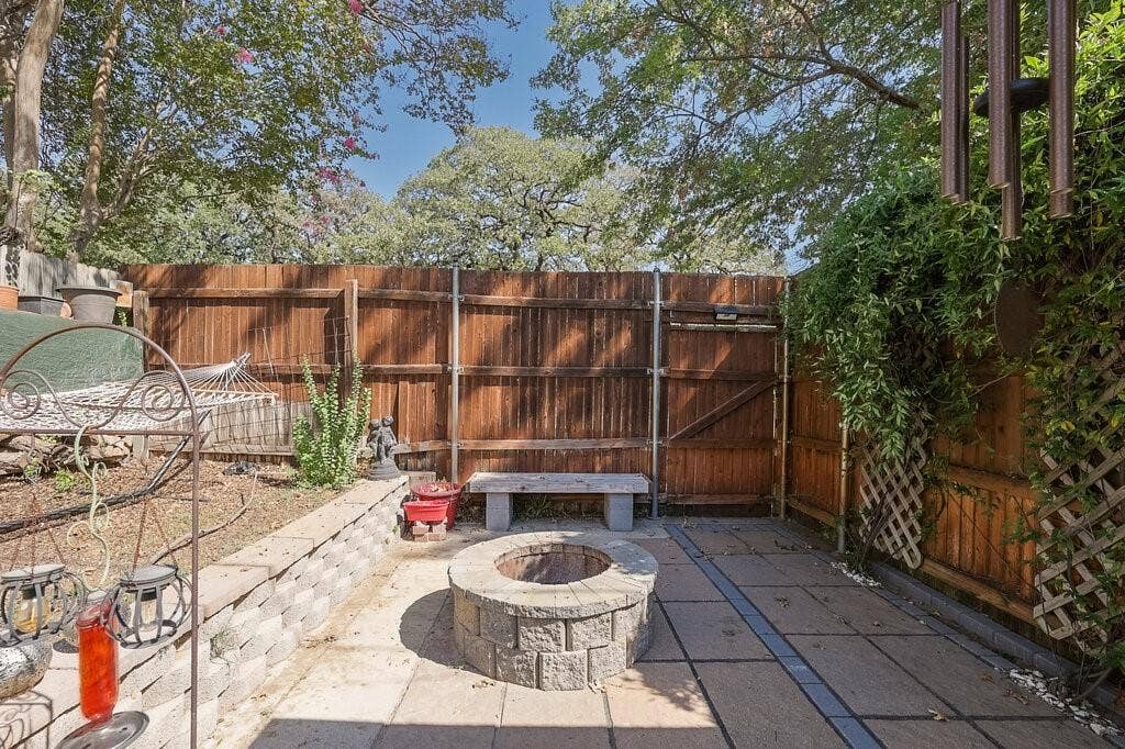 Outdoor space featuring a paved stone patio, built-in circular fire pit, raised stone retaining wall, and wood privacy fencing