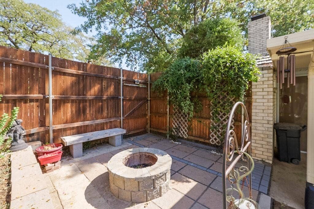 Paved stone patio featuring a circular masonry fire pit, built-in masonry seating, wooden privacy fencing, and decorative lattice wall panels