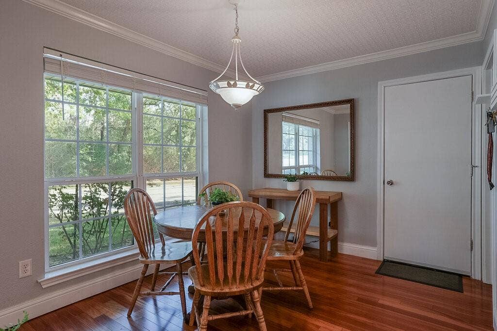 Room featuring wood-finish flooring, crown molding, a multi-pane window, and a central pendant light fixture