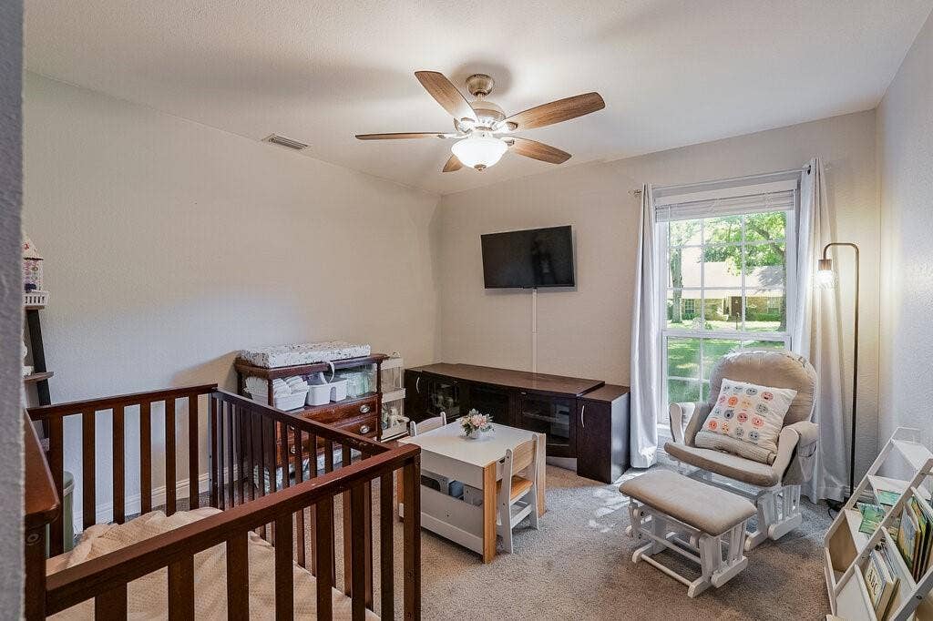 Neutral-toned bedroom featuring carpeted flooring, a multi-pane window with natural light, and a ceiling fan with integrated light fixture