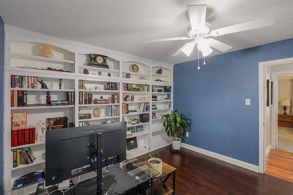 Custom floor-to-ceiling built-in white shelving, wood-finish flooring, and a multi-blade ceiling fan with integrated lighting
