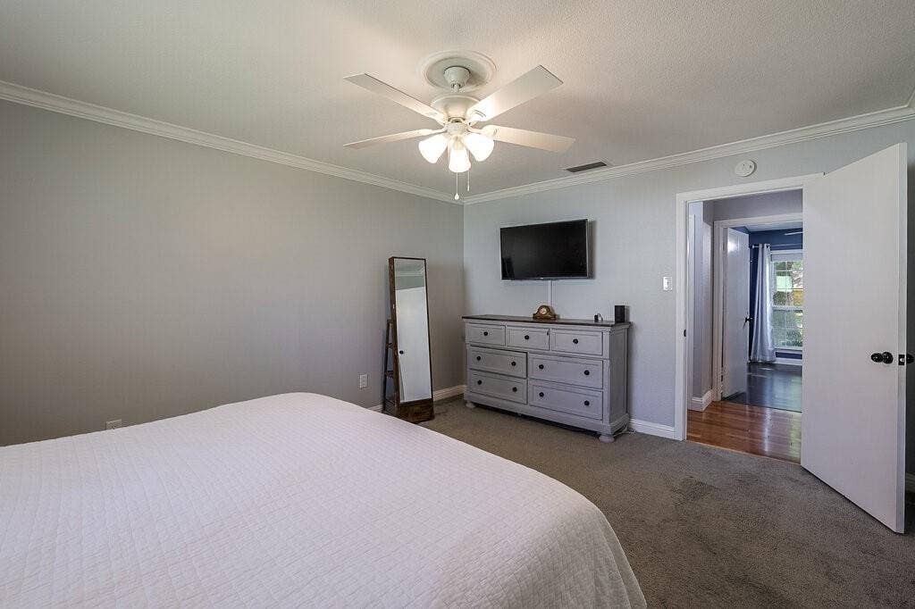 Neutral wall tones complemented by crown molding, wall-to-wall carpeting, and a central ceiling fan with integrated lighting