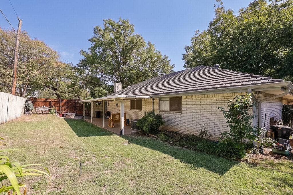 Brick exterior residence featuring a covered patio, a hipped roof with tile shingles, and a fenced backyard