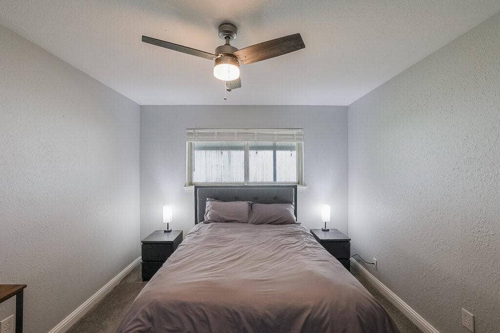 Neutral-toned interior featuring carpeting, a horizontal sliding window with blinds, and a modern ceiling fan with an integrated light fixture