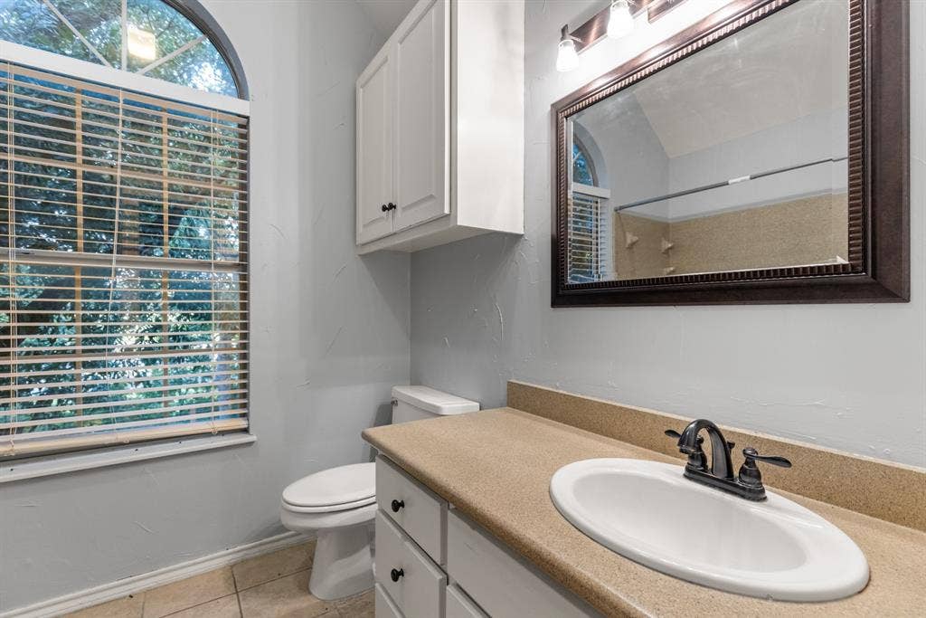 207 Westlane Circle, Woodway, TX 76712 Bathroom featuring an arched window, white cabinetry with built-in wall storage, solid surface countertop with integrated oval sink, and a framed mirror