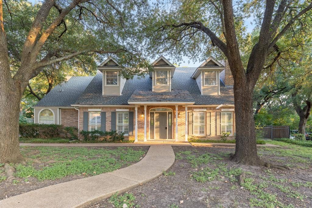 207 Westlane Circle, Woodway, TX 76712 Brick and siding exterior featuring three gabled dormers, an arched covered entryway, shuttered windows, and mature trees on the grounds