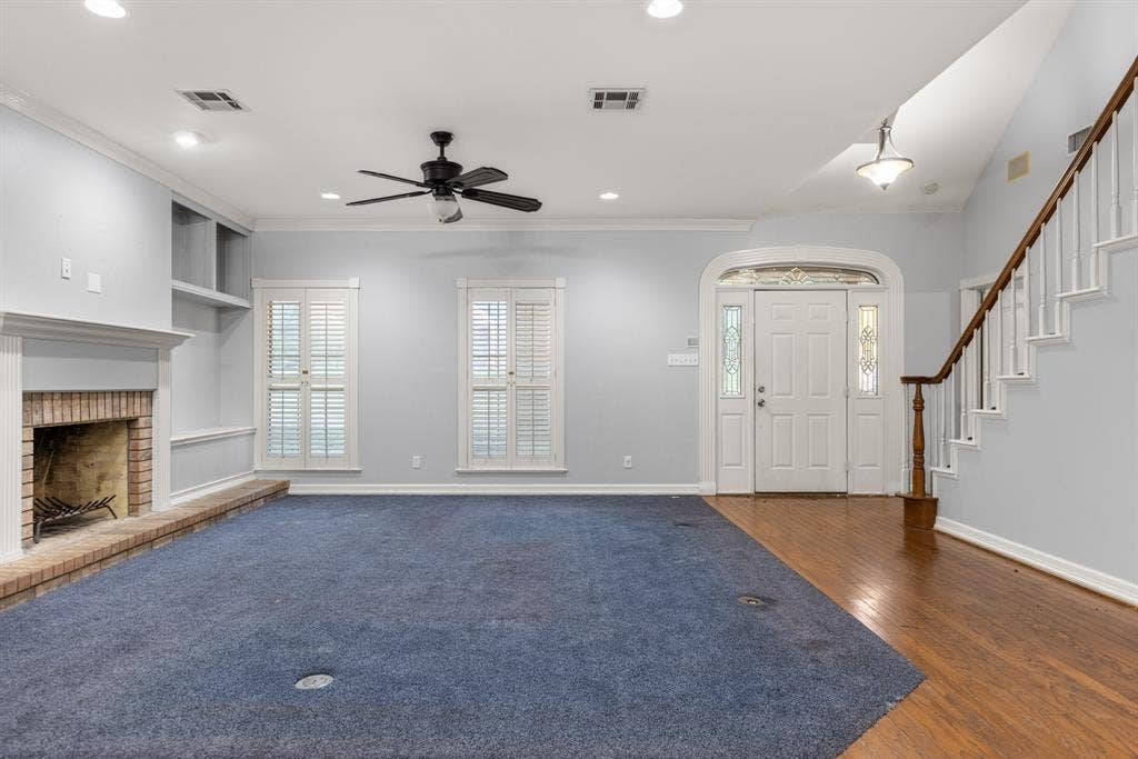 207 Westlane Circle, Woodway, TX 76712 Living area featuring a masonry fireplace with a raised brick hearth, recessed ceiling lighting, built-in shelving, plantation shutters, and a staircase with a wooden handrail