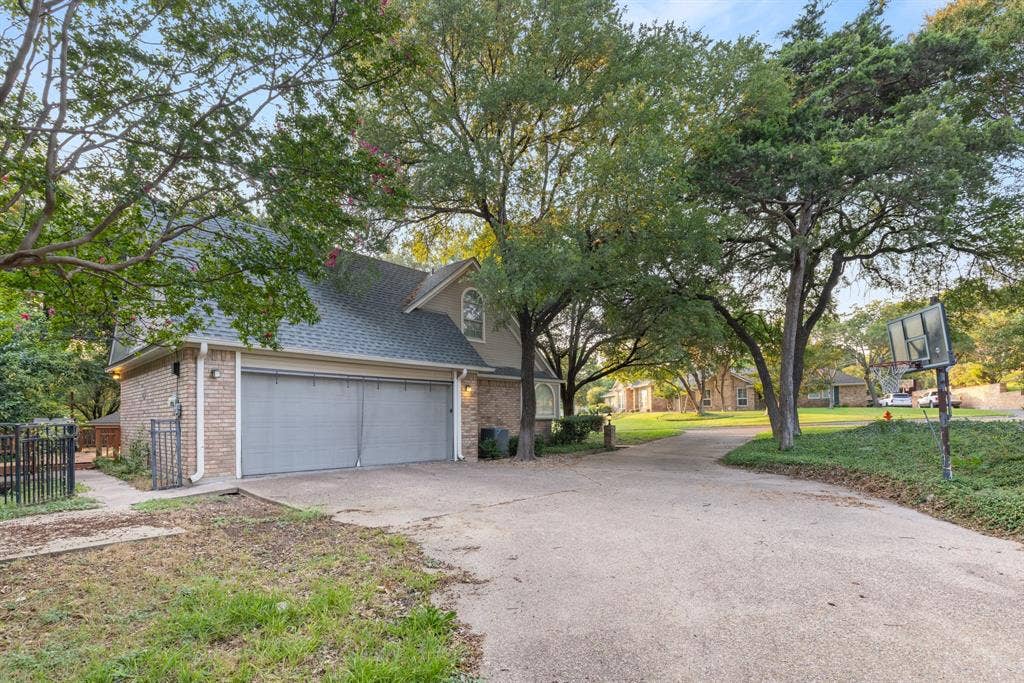 207 Westlane Circle, Woodway, TX 76712 Brick exterior with a detached two-car garage, steep-pitched roofline, expansive concrete driveway, and mature landscaping