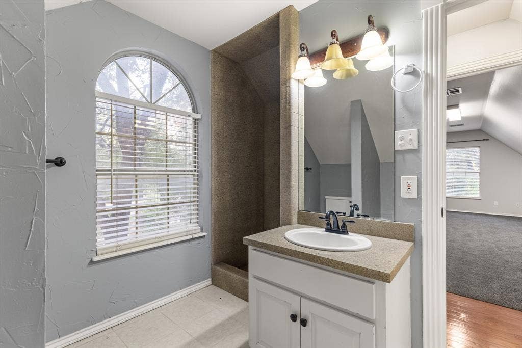 207 Westlane Circle, Woodway, TX 76712 Bathroom featuring a vanity with a solid-surface countertop, an integrated oval sink, a wall-mounted light fixture, and an arched window