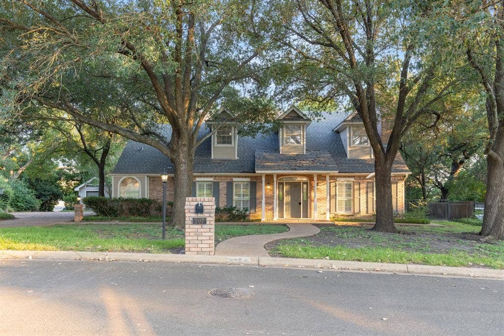 207 Westlane Circle, Woodway, TX 76712 Two-story brick exterior featuring a steeply pitched roof, dormer windows, covered front entrance with columns, and mature canopy trees