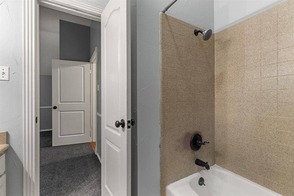 207 Westlane Circle, Woodway, TX 76712 Bathroom featuring a shower and tub combination with matte black fixtures, textured tile surround, and arched-panel interior doors