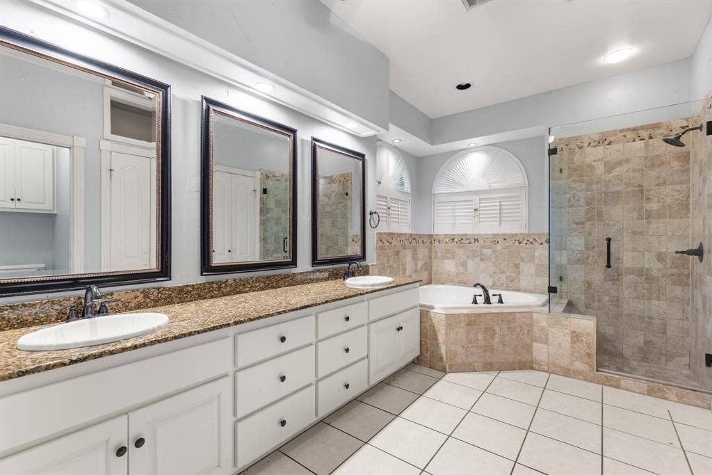 207 Westlane Circle, Woodway, TX 76712 Dual vanity with white cabinetry and stone countertops, oversized framed wall mirrors, corner soaking tub with tile surround, and walk-in glass-enclosed shower