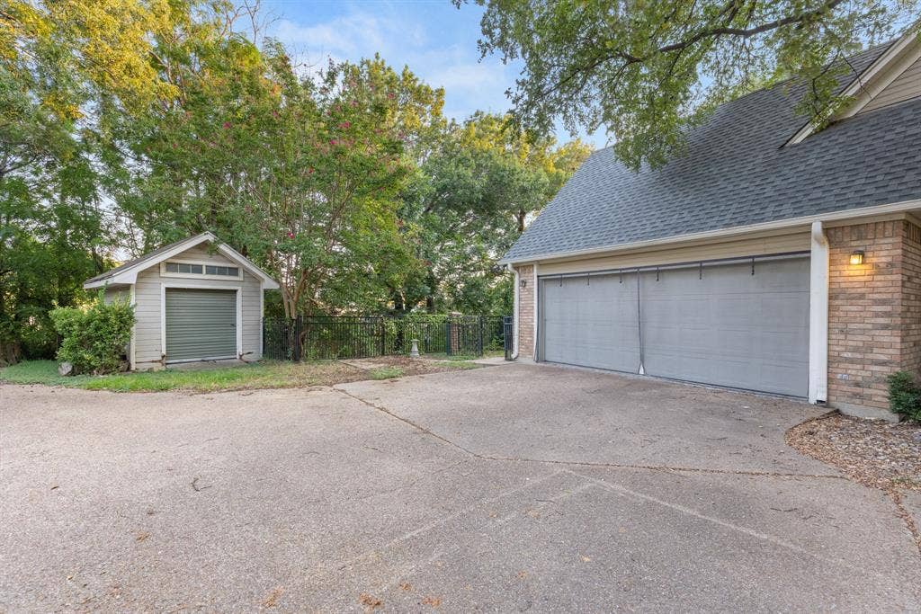 207 Westlane Circle, Woodway, TX 76712 Attached two-car garage with brick and siding exterior, concrete driveway, and detached storage building featuring a roll-up door