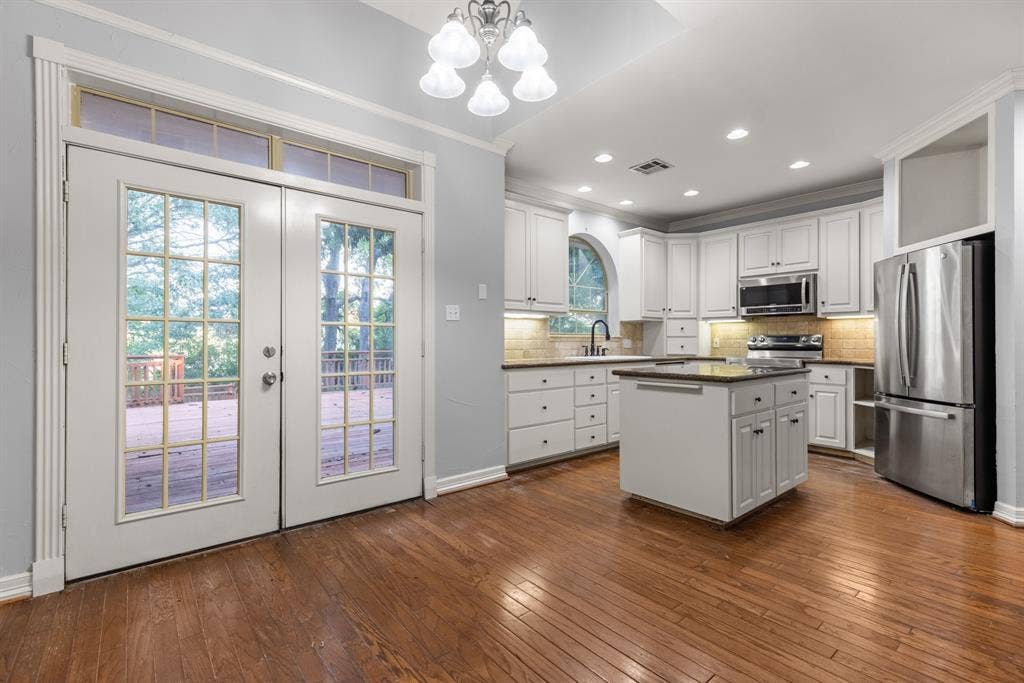 207 Westlane Circle, Woodway, TX 76712 Kitchen featuring white cabinetry, center island with stone countertop, stainless steel appliances, wood-finish flooring, and French doors with transom windows