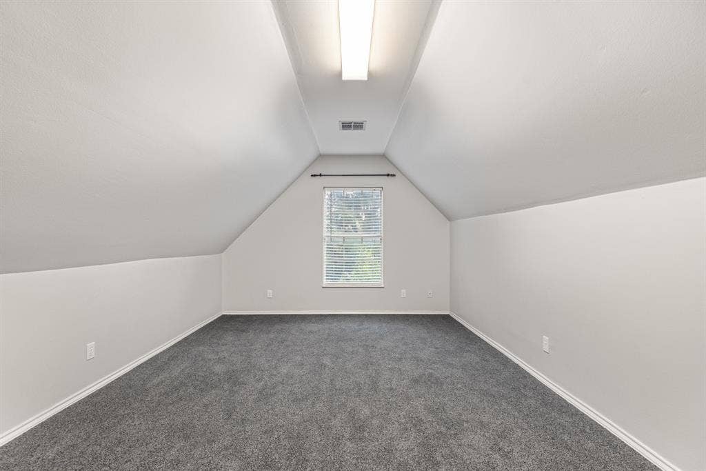 207 Westlane Circle, Woodway, TX 76712 Vaulted ceiling featuring neutral wall paint, gray carpeting, a centrally located linear flush-mount light fixture, and a single window with blinds