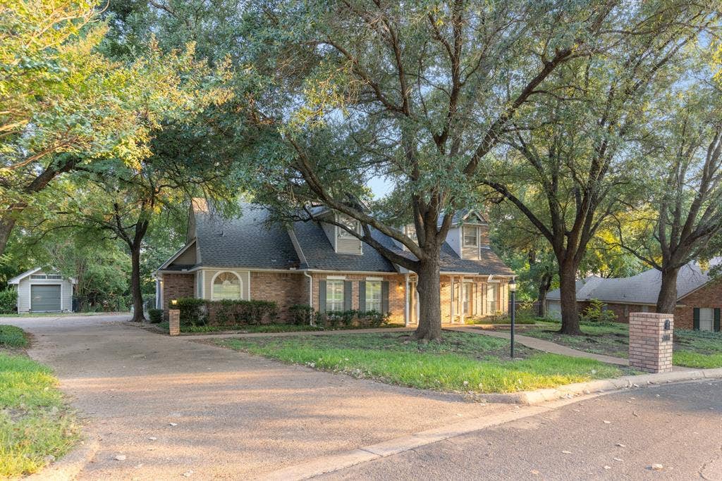 207 Westlane Circle, Woodway, TX 76712 Multi-story brick exterior featuring a steep-pitched roof, dual dormer windows, an arched window detail, and a detached garage structure