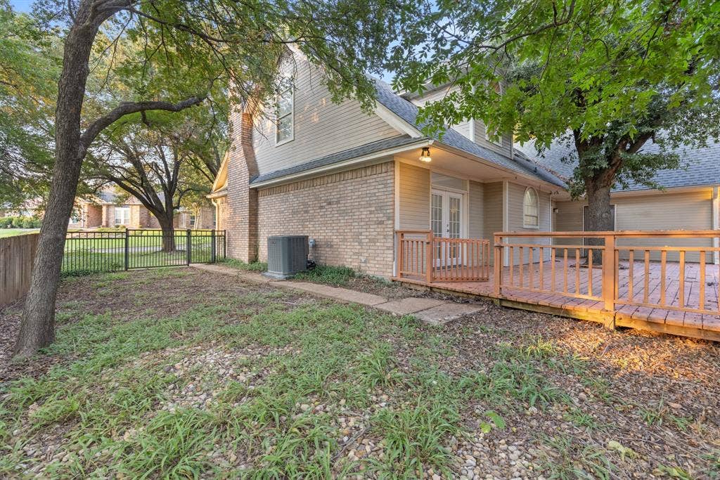 207 Westlane Circle, Woodway, TX 76712 Exterior featuring a brick and siding facade, raised wood deck with railing, metal perimeter fencing, and mature trees